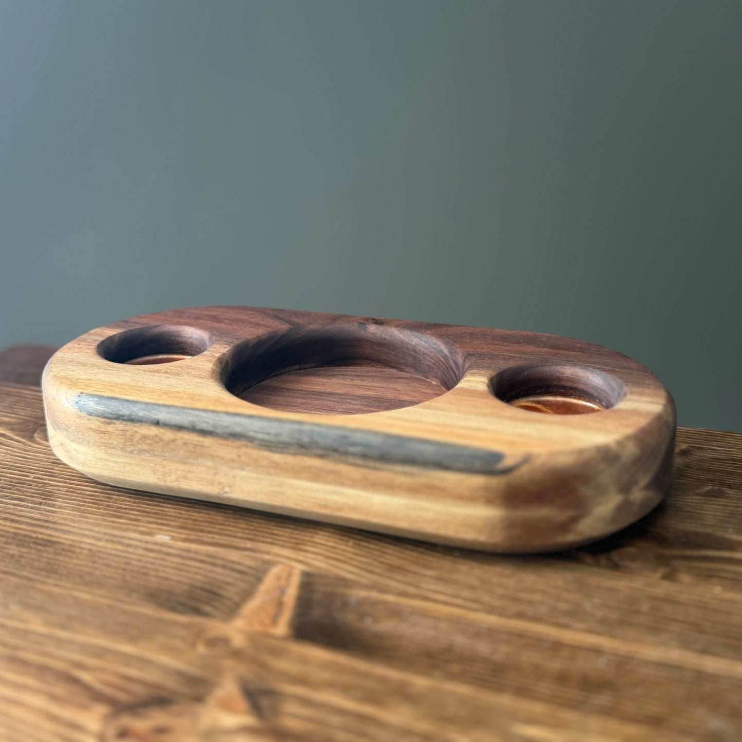 Handcrafted hardwood whiskey display tray with three recessed holders and dark accent inlay, shown empty on a wooden table against a neutral background.