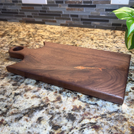 Walnut cutting board on a granite countertop with a plant in the background