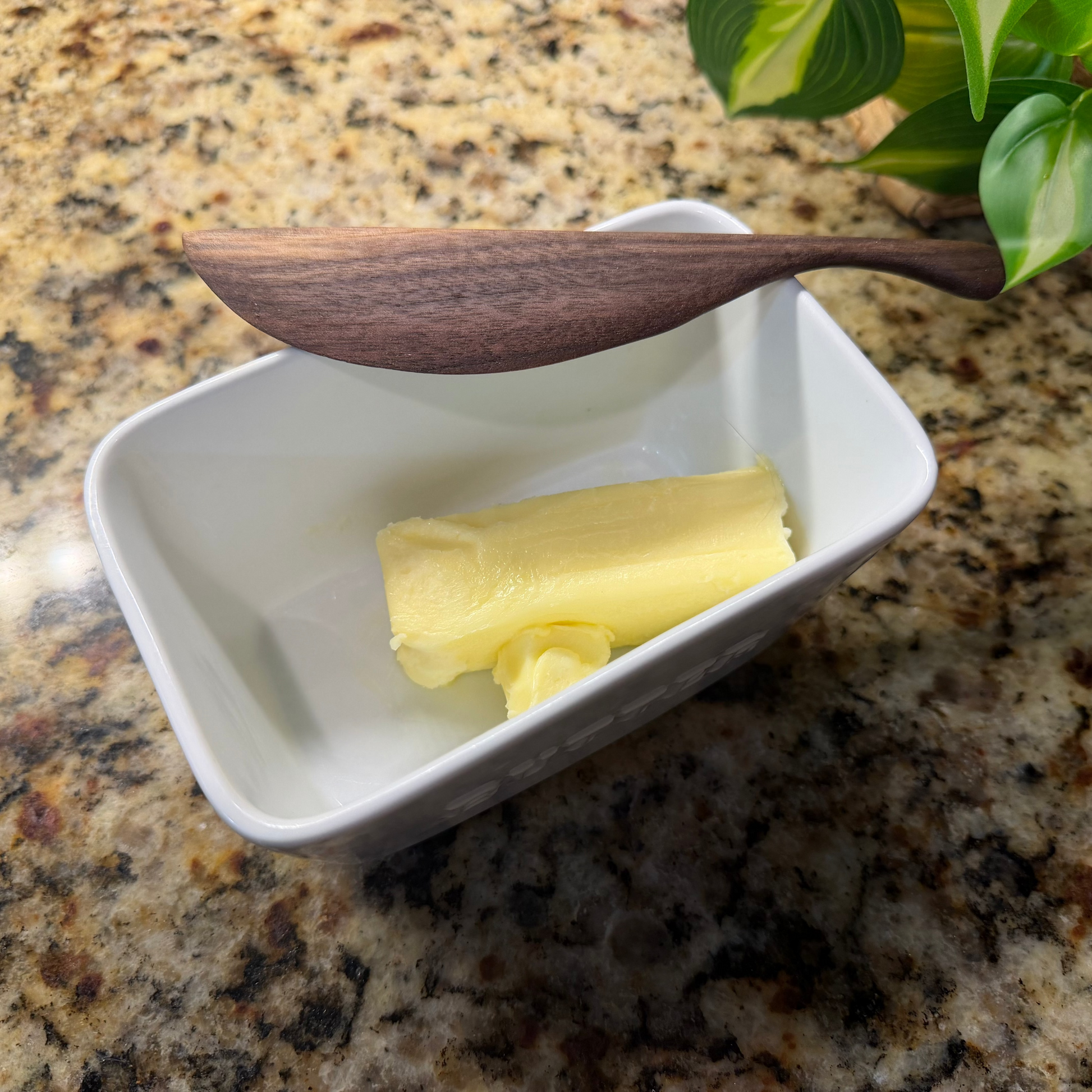 Walnut butter knife on a white dish on a granite countertop