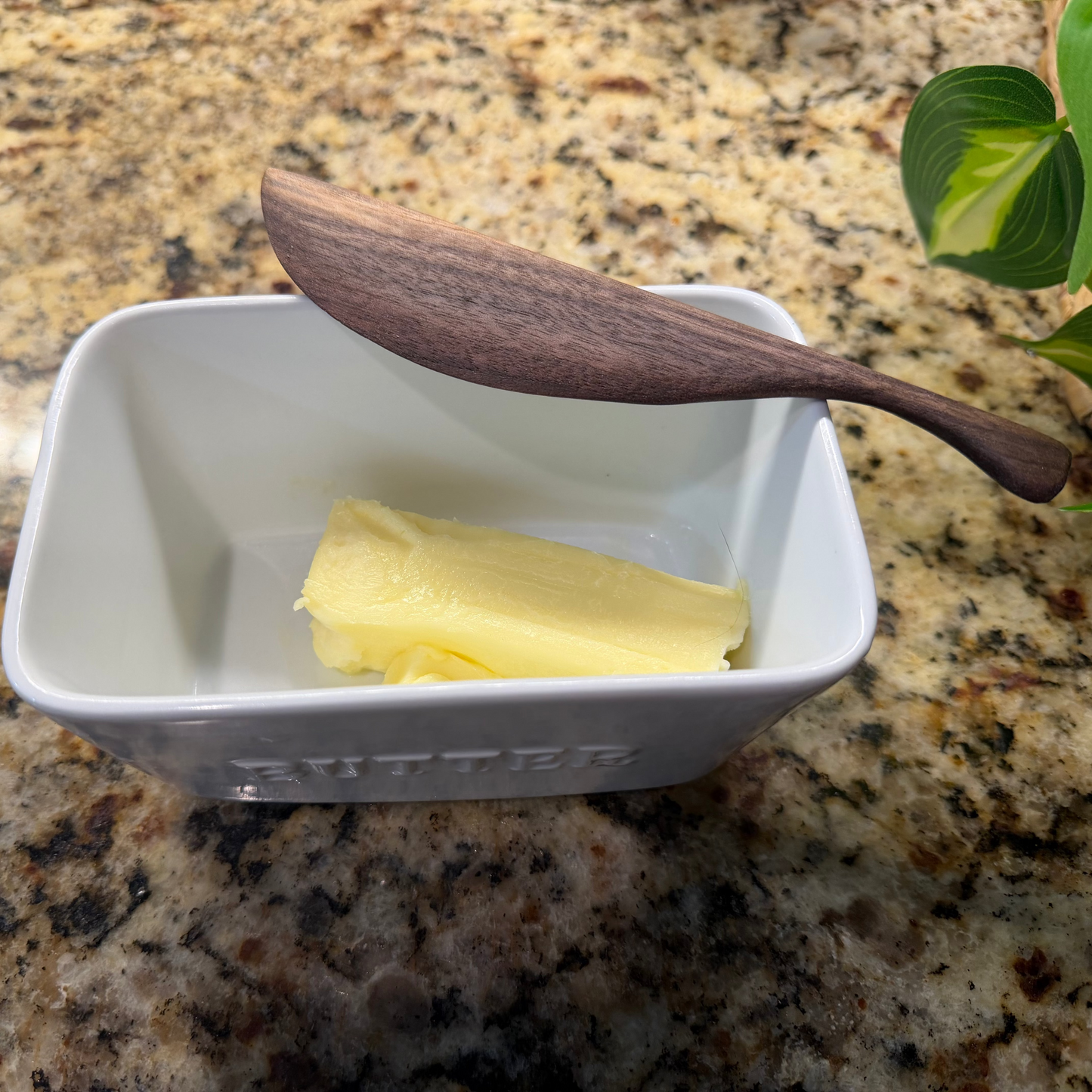 Walnut butter knife on a butter dish on a granite countertop