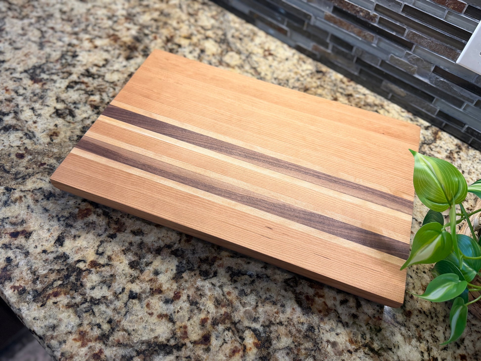 Cherry cutting board with a walnut and white oak striped pattern on a granite countertop