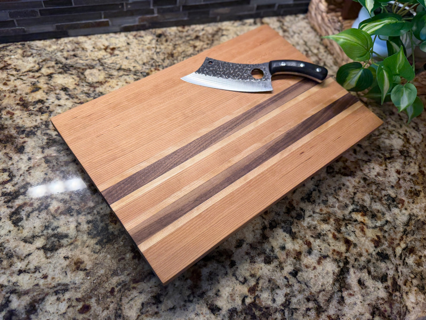 Cherry, walnut, and white oak cutting board with a knife on a granite countertop