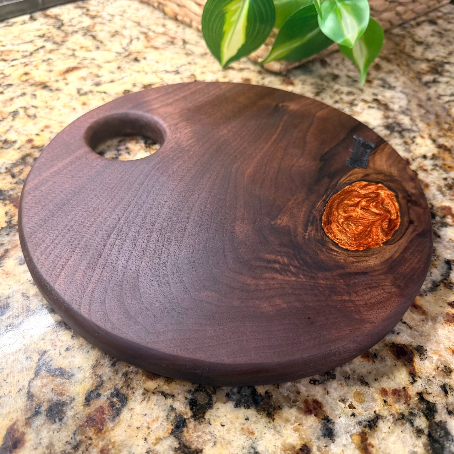 Round walnut charcuterie board with a copper epoxy filled knot on a granite countertop